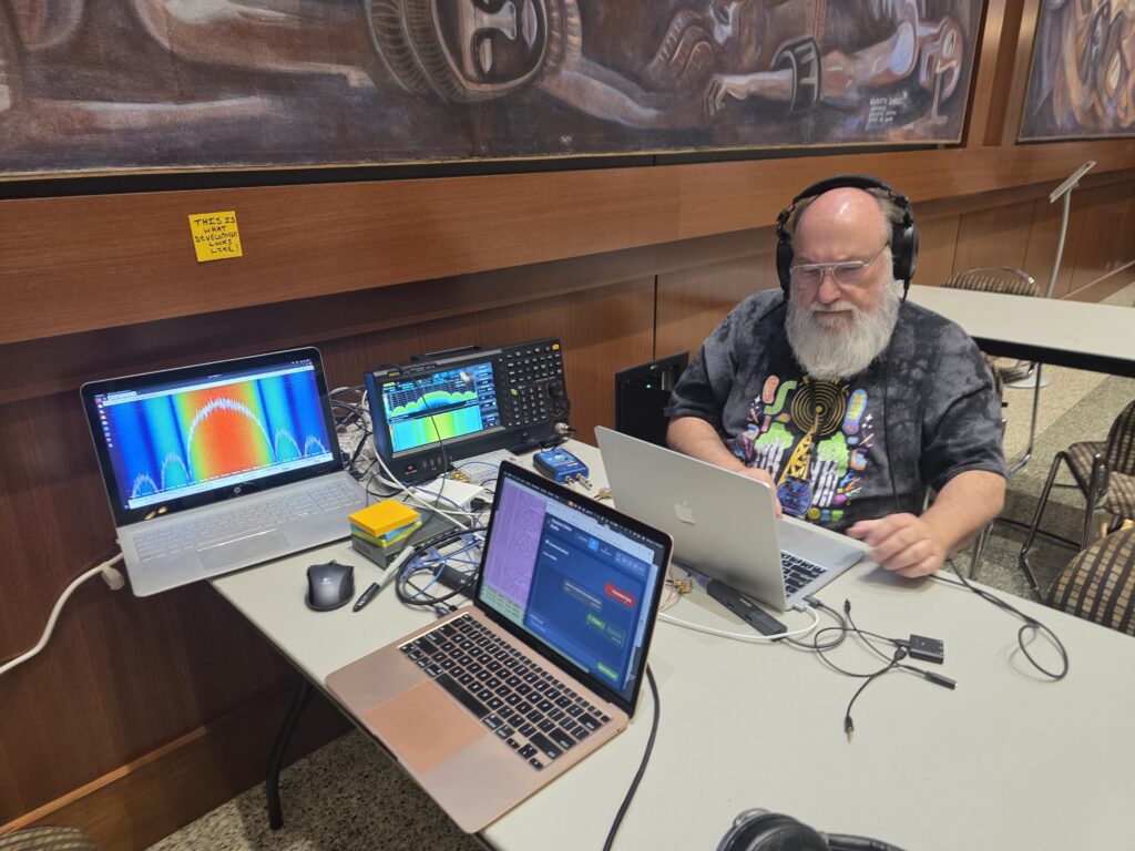 BSides San Diego 2026 RF Village Opulent Voice Development station staffed by Paul Williamson KB5MU. The post it note on the wall says "This is what development looks like!"